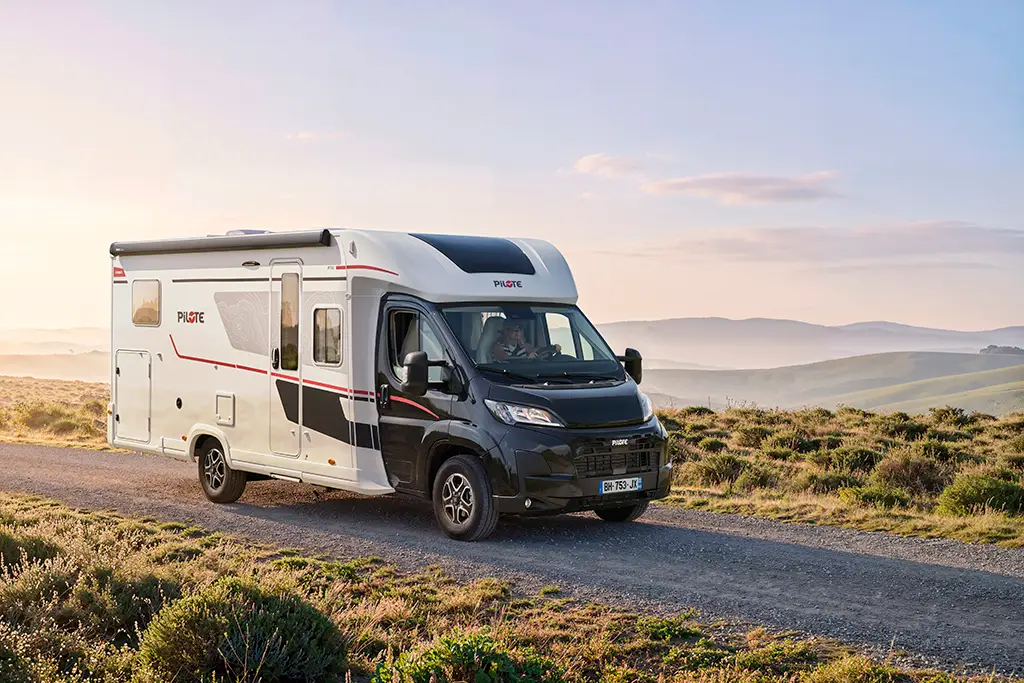 Camping-car profilé Pilote dans un paysage de collines au lever du jour